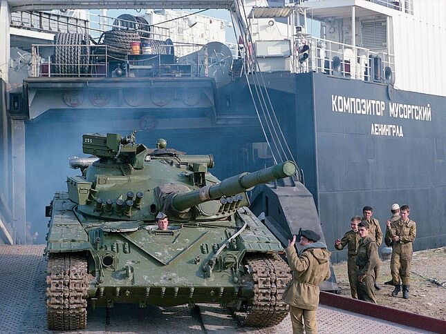 Im Rahmen des Abzugs der sowjetischen Truppen aus der  DDR wird im September 1990 in Rostock ein Panzer auf das Transportschiff „Komponist Mussorgski“ verladen. Der Panzer fährt rückwärts über eine Rampe in den Frachtraum, an der Seite stehen sowjetische Soldaten.