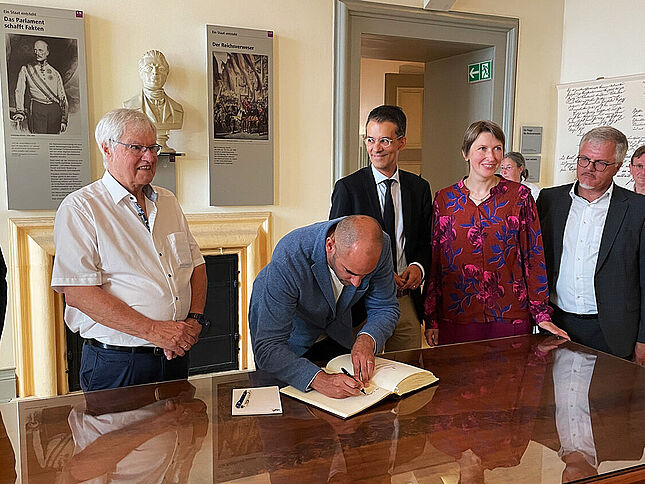 Dr. Danyal Bayaz (Bildmitte) trägt sich in das Gästebuch der Bundesarchiv-Erinnerungsstätte ein Bild wie sich Dr. Danyal Bayaz (Bildmitte) in das Gästebuch der Bundesarchiv-Erinnerungsstätte Rastatt einträgt