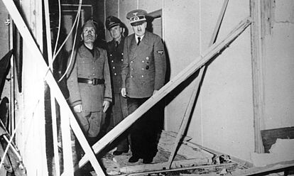 Besichtigung der zerstörten Barracke auf der Wolfschanze durch Benito Mussolini (links) und Adolf Hitler (rechts). Im Hintergrund ist Dolmetscher Dr. Paul Schmidt zu sehen