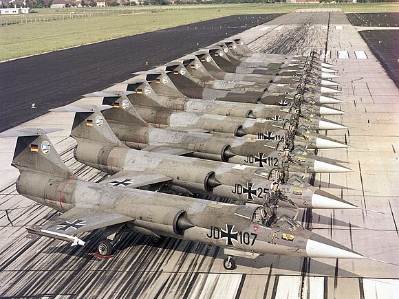 Zwölf F-104G „Starfighter“ des Jagdgeschwaders 74 „Mölders“ stehen nebeneinander auf einer Startbahn.