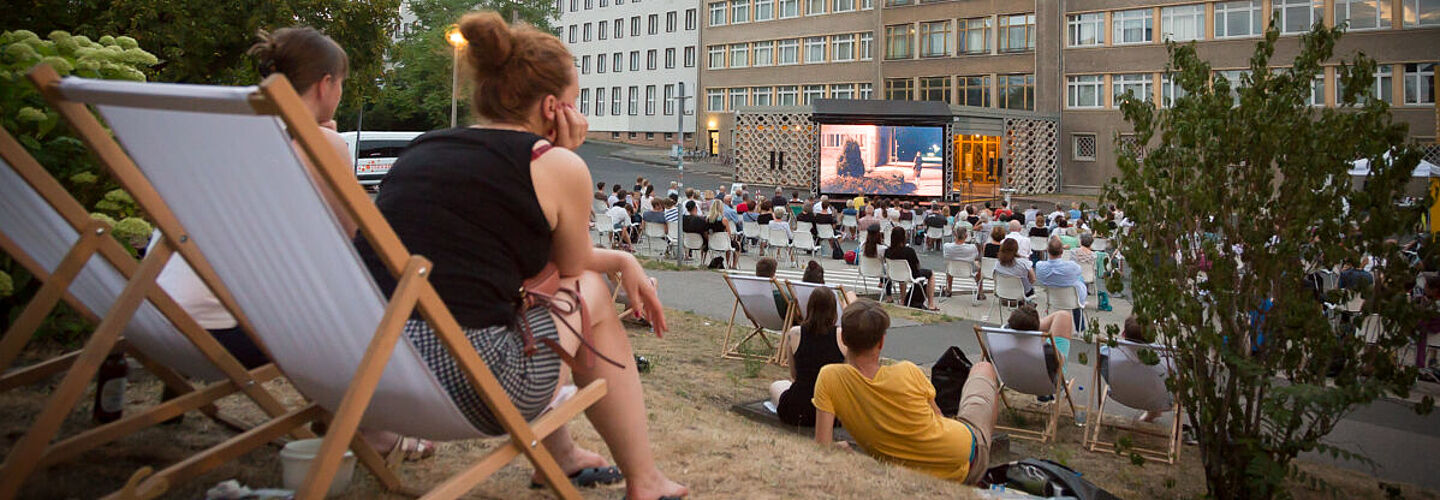 Im Innenhof der ehemaligen Stasi-Zentrale sitzen Menschen, die auf einen großen Kinobildschirm schauen.