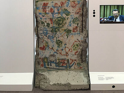 Ein Segment der Berliner Mauer in der Dauerausstellung in Rastatt. Daneben hängt ein Bildschirm, auf dem Günter Schabowski zu sehen ist.