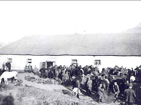 Reiter mit ihren Pferden während einer Rast vor einem Stall.