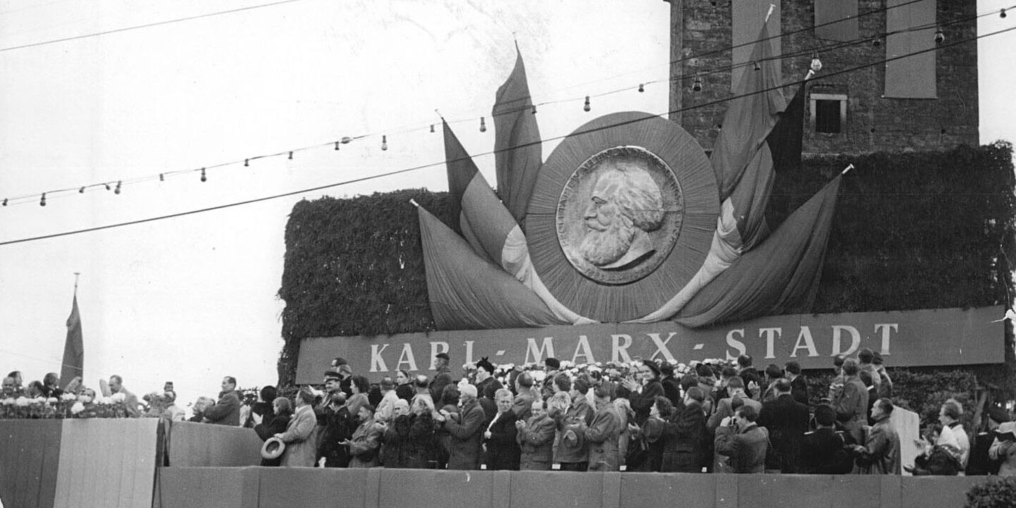 Menschen auf einer Tribüne während der Feierlichkeiten am 11. Mai 1953 im Rahmen der Umbenennung von Chemnitz in Karl-Marx-Stadt, Quelle:
            BArch, Bild 183-19540-0009 / Krueger