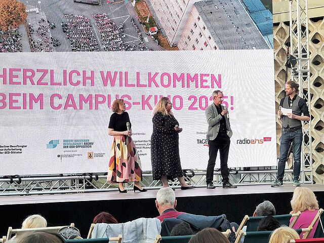 Moderator mit drei Gästen auf der Bühne