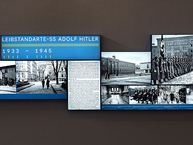 Beleuchtete Fotos und Texte sind an eine Wand montiert.