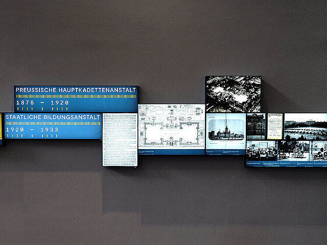 Beleuchtete Fotos und Texte sind an eine Wand montiert.