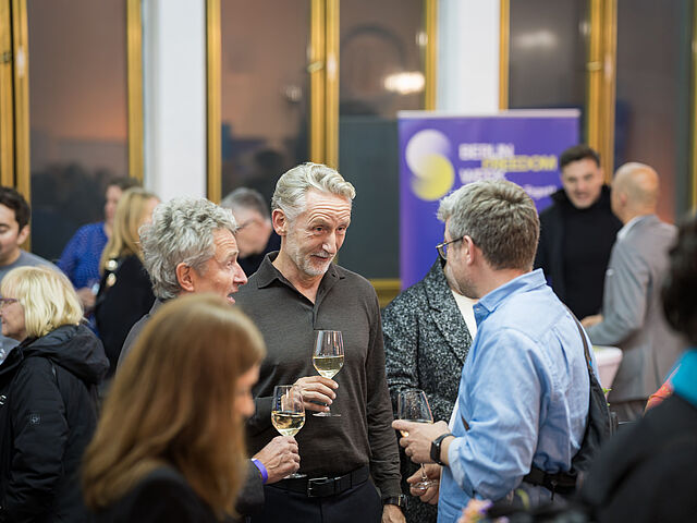 Mehrere Personen sind zu sehen. Sie halten Weingläser in ihren Händen.