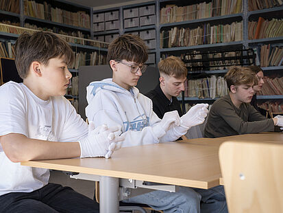Eine Gruppe von fünf Jungen sitzt nebeneinander an einem Tisch. Die Jungen ziehen weiße Handschuhe an.