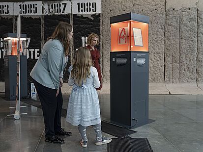 Zwei Personen stehen vor einer Objektstele in der Ausstellung "Alles Wissen Wollen".