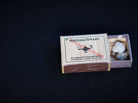 Streichholzschachtel Das Bild zeigt eine geöffnete Streichholzschachtel, in der einige kleine Steine liegen.