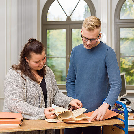 Zwei Mitarbeitende im Bundesarchiv blättern in Dokumenten