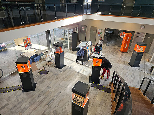 Zu Gast im Staatsarchiv Bremen, 24. September 2026 Vogelperspektive: in einem hohen Saal werden Kisten transortiert. Einige Ausstellungsstelen stehen schon.