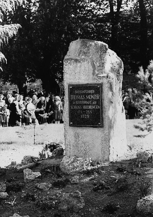 Gedenkstein mit der Aufschrift "Bauernführer Thomas Müntzer in Kerkerhaft auf Schloss Heldrungen 17.5.–23.5.1525". Im Hintergrund stehen mehrere Menschen.