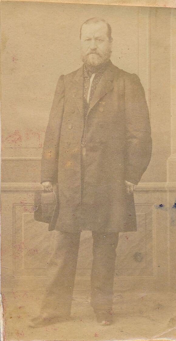 Porträtfoto von Daniel Heinrich Saul, der vor einer Wand steht und einen Hut in der Hand hält.