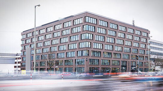 Ein viereckiges Gebäude mit zahlreichen Fenstern an einer Straße
