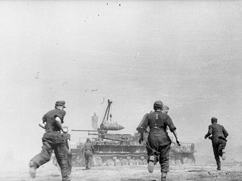 Mehrere deutsche Soldaten rennen zu einem Mörser, der gerade mit einem Geschoss beladen wird.