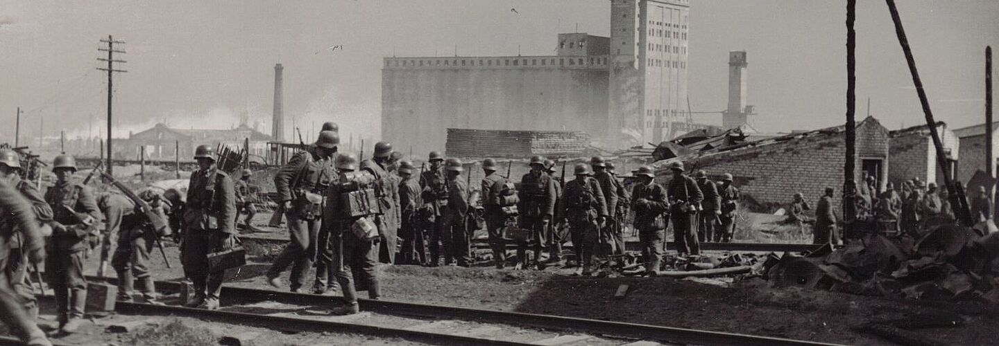Deutsche Soldaten in Stalingrad, September 1942 Schwarz-Weiß-Aufnahme von Soldaten mit Ausrüstung beim Überqueren von Bahngleisen vor zerstörten Gebäuden