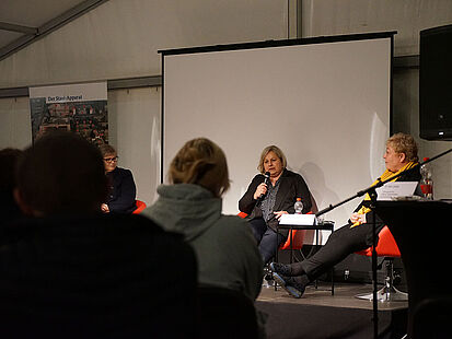 Die Vizepräsidentin im Bundesarchiv für das Stasi-Unterlagen-Archiv Alexandra Titze sitzt während eines Podiumsgesprächs mit einem Mikrofon in der Hand auf der Bühne. Neben ihr sind die Bundesbeauftragte für die Opfer der SED-Diktatur Evelyn Zupke und die Beauftrage des Landes Sachsen-Anhalt zur Aufarbeitung der SED-Diktatur Birgit Neumann-Becker zu sehen, im Vordergrund sitzen Zuschauerinnen und Zuschauer.