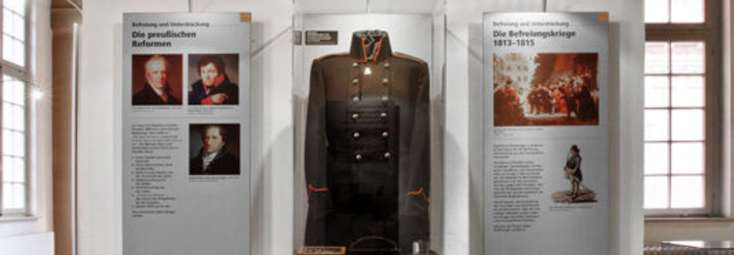 Die schwarz-rote Fahne der Jenenser Urburschenschaft hängt über einer Glasvitrine mit dem dunklen Uniformrock eines Lützower Jägers.