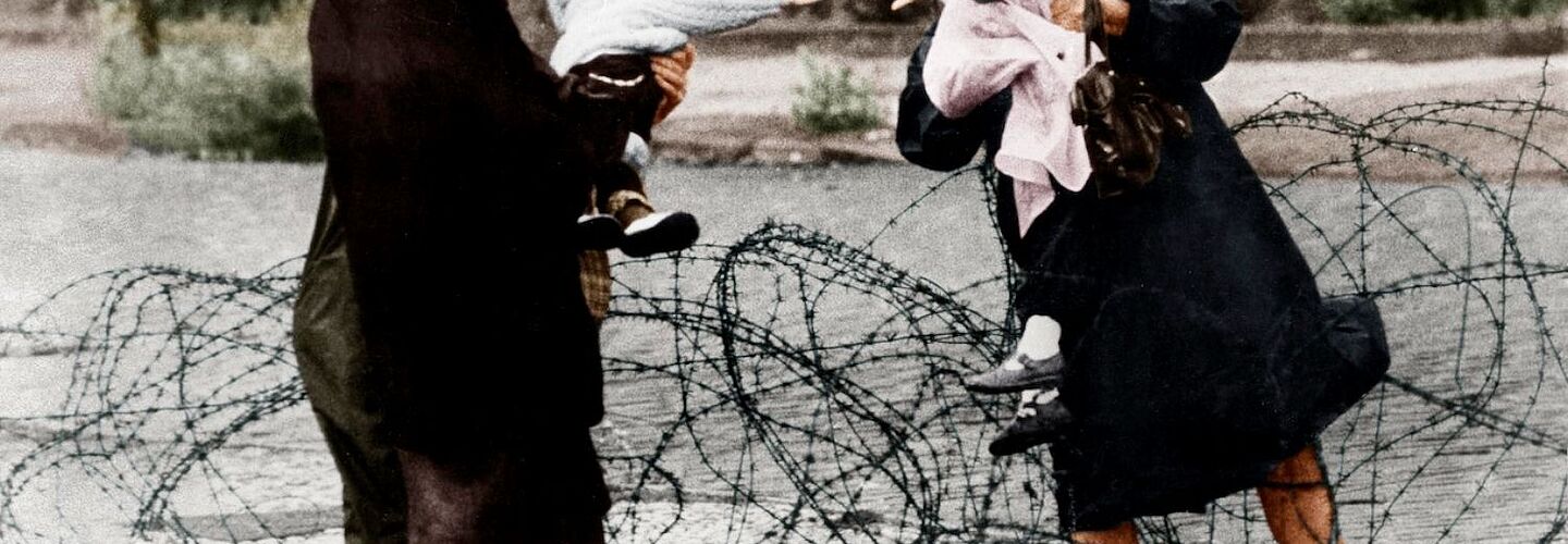 Zwei Frauen unterhalten sich, Stacheldraht liegt über die provisorische Grenzmauer.