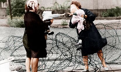 Zwei Frauen unterhalten sich, Stacheldraht liegt über die provisorische Grenzmauer.