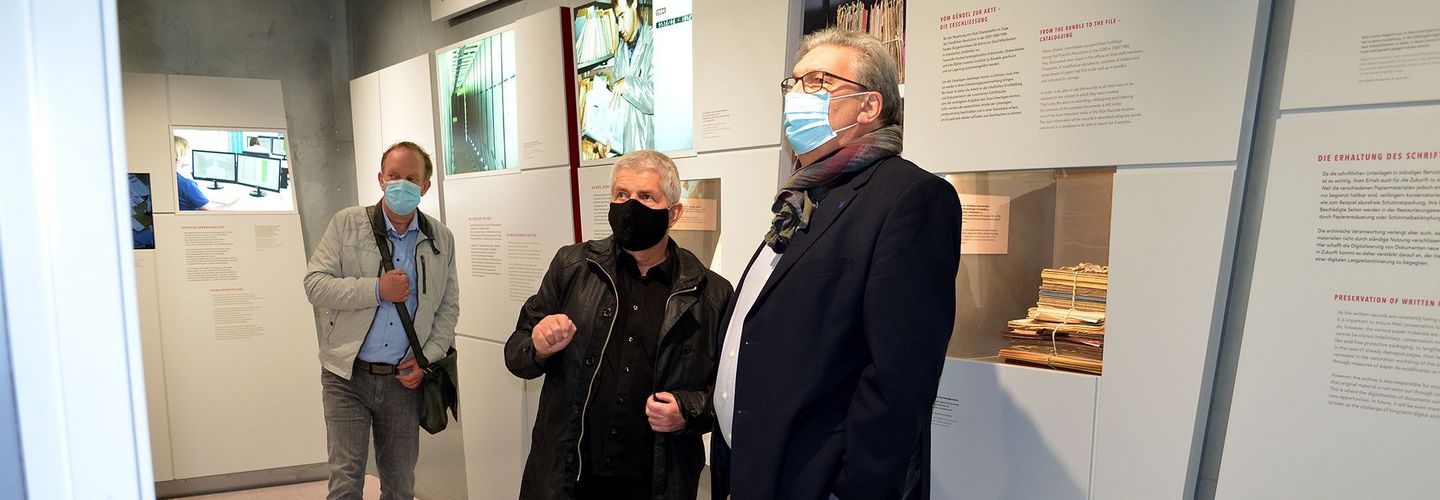 Der Berliner Aufarbeitungsbeauftragte Tom Sello, der Bundesbeauftragte Roland Jahn und der Präsident des Abgeordnetenhauses von Berlin, Ralf Wieland stehen in der Ausstellung 'Einblick ins Geheime' und schauen auf eine Ausstellungstafel. Alle drei Männer tragen einen Mund-Nasen-Schutz.
