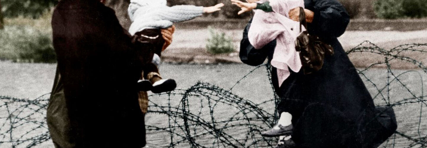 Zwei Frauen unterhalten sich, Stacheldraht liegt über der provisorischen Grenzmauer.