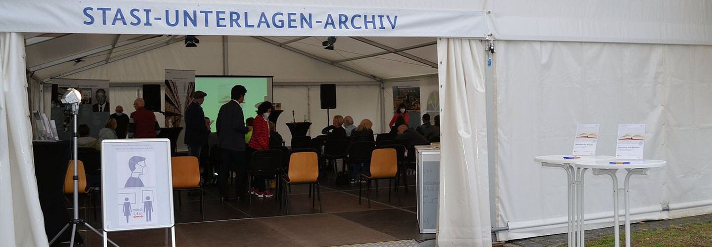 Festzelt für die EinheitsEXPO 2021 in Halle mit der Aufschrift 'Stasi-Unterlagen-Archiv'. Im Innern befinden sich stehende und sitzende Besucherinnen und Besucher