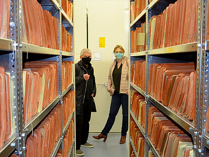 Das Bild zeigt den Bundesbeauftragten Roland Jahn und die Bundestagsabgeordnete Melanie Bernstein am Ende eines Regals, in welchem sich Stasi-Akten befinden.
