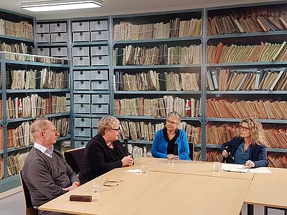 Vier Personen sitzen um einen Tisch. Es sind von links nach rechts:&nbsp;Stefan Trobisch-Lütge, Evelyn Zupke​​​​​​​, Ulrike Poppe und Dagmar Hovestädt. Im Hintergrund sieht man eine Wand, die vollständig mit einer Fototapete mit Regalen voller Stasiakten beklebt ist.