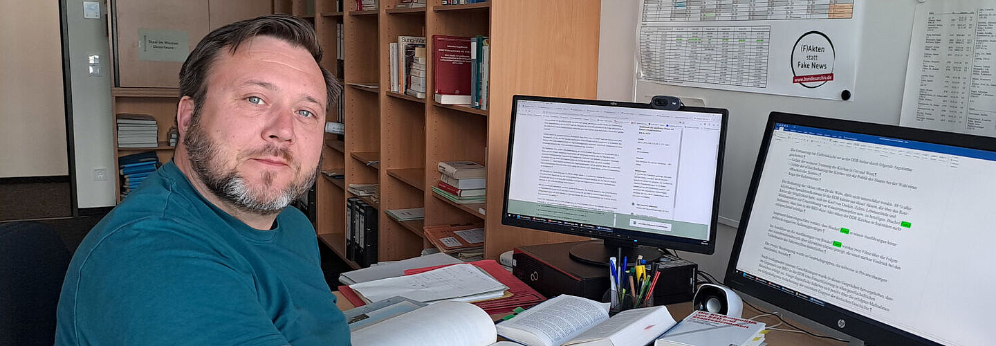 Martin Stief sitzt an einem Schreibtisch vor zwei Monitoren und blickt in die Kamera.