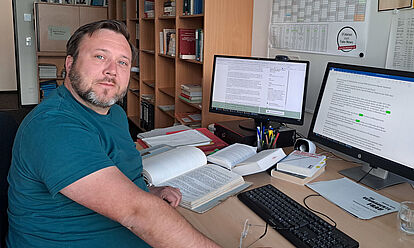 Martin Stief sitzt an einem Schreibtisch vor zwei Monitoren und blickt in die Kamera.