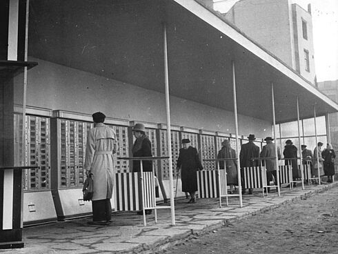 Mehrere Menschen stehen vor Automaten unter einer Überdachung.