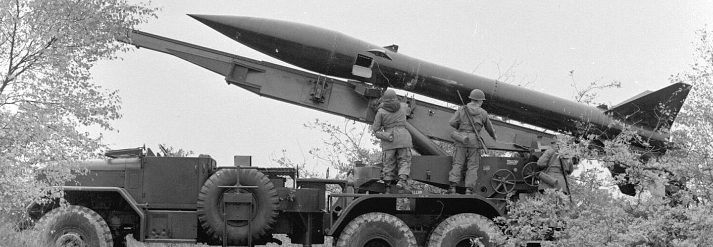 Seitenansicht eines LKWs mit einer Raketenstartvorrichtung. Auf der Startvorrichtung liegt eine MGR-1 Kurzstreckenrakete. Vor der Rakete stehen Soldaten der Bundeswehr.