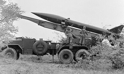 Seitenansicht eines LKWs mit einer Raketenstartvorrichtung. Auf der Startvorrichtung liegt eine MGR-1 Kurzstreckenrakete. Vor der Rakete stehen Soldaten der Bundeswehr.