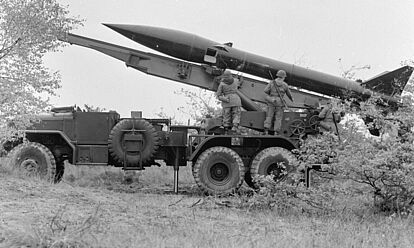 Seitenansicht eines LKWs mit einer Raketenstartvorrichtung. Auf der Startvorrichtung liegt eine MGR-1 Kurzstreckenrakete. Vor der Rakete stehen Soldaten der Bundeswehr.