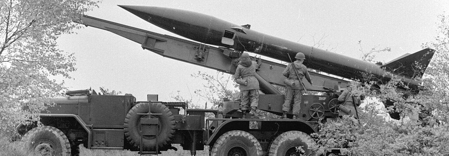 Seitenansicht eines LKWs mit einer Raketenstartvorrichtung. Auf der Startvorrichtung liegt eine MGR-1 Kurzstreckenrakete. Vor der Rakete stehen Soldaten der Bundeswehr.