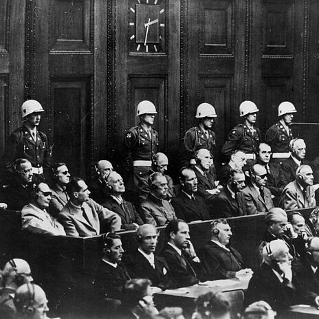 Anklagebank beim Nürnberger Hauptkriegsverbrecherprozess, 1946 Blick auf die Anklagebank beim Nürnberger Prozess. Zu sehen sind die Hauptkriegsverbrecher Karl Dönitz, Erich Raeder, Baldur von Schirach, Fritz Sauckel, Alfred Jodl, Franz von Papen, Arthur Seyß-Inquart, Albert Speer, Konstantin von Neurath, Hans Fritsche, Hermann Göring, Rudolf Hess, Joachim von Ribbentrop, Wilhelm Keitel, Ernst Kaltenbrunner, Alfred Rosenberg, Hans Frank, Wilhelm Frick, Julius Streicher, Walter Funk und Hjalmar Schacht. Hinter den Angeklagten stehen amerikanische Militärpolizisten mit weißen Helmen.