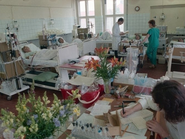 Liegende Patienten an Dialysemaschinen und eine Schwester bei Schreibarbeiten in der Dialyseabteilung der Klinik für Innere Medizin in Rostock, 1988 
