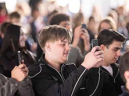 Tag der Pressefreiheit 2026 Viele sitzende Personen sind zu sehen. Einige davon halten ihre Smartphones hoch.