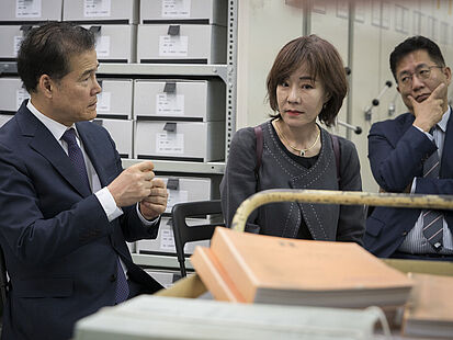 Kim Yung Ho sitzt auf einem Stuhl im Magazin des Stasi-Unterlagen-Archivs. Vor ihm liegen Akten.