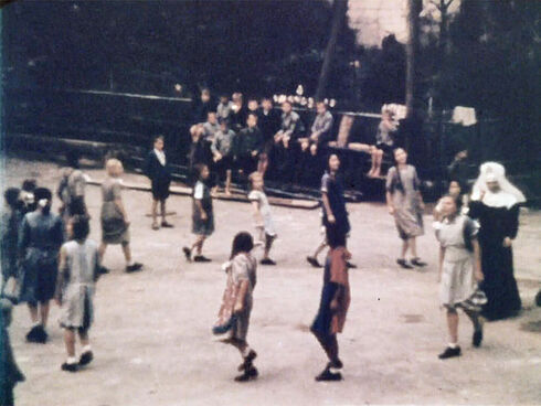 Standbild aus einem farbigen Dokumentarfilm mit im Kreis gehenden Mädchen und einer Nonne