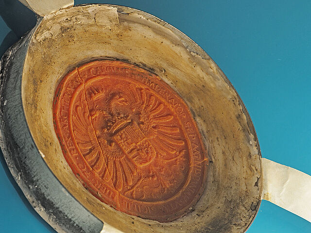 Nachaufnahme eines Wachssiegels mit gelbem Rand und roter Mitte auf blauem Hintergrund