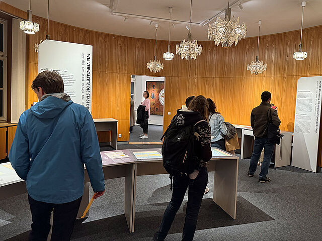 Menschen in einem holzgetäfelten Raum mit Ausstellungstischen