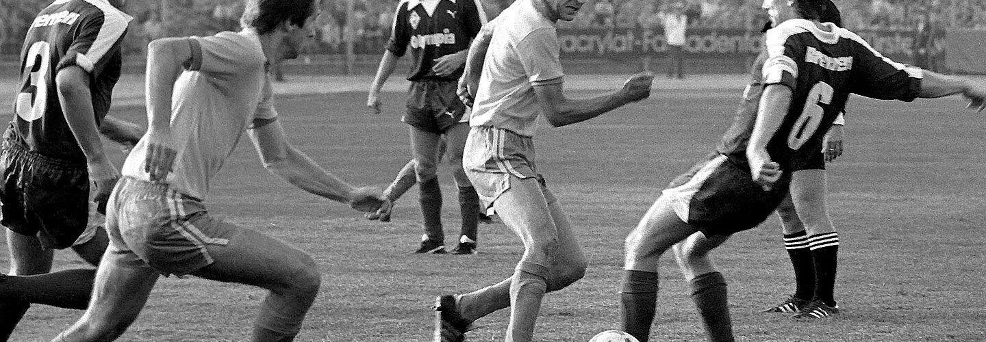Zu sehen sind fünf Fußballspieler, die um einen Ball dribbeln.