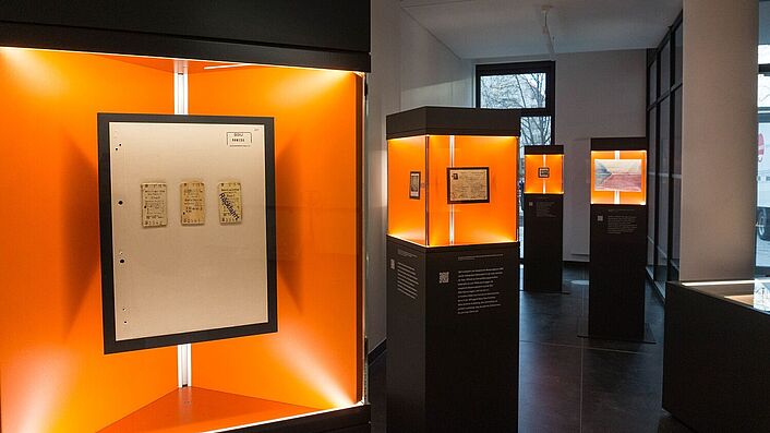 Blick in die Wanderausstellung. Zu sehen sind mehrere Stelen mit Glasvitrinen, in denen sich Dokumente, Fotos und Objekte befinden.