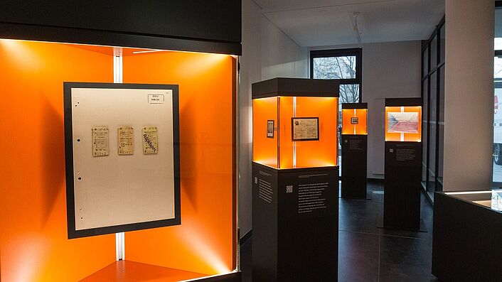 Blick in die Wanderausstellung. Zu sehen sind mehrere Stelen mit Glasvitrinen, in denen sich Dokumente, Fotos und Objekte befinden.