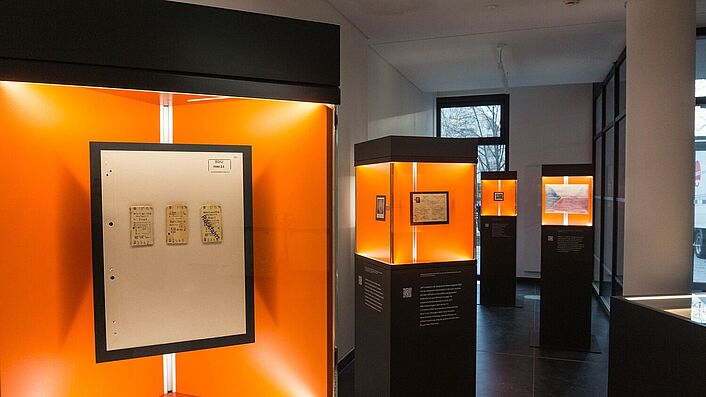 Blick in die Wanderausstellung. Zu sehen sind mehrere Stelen mit Glasvitrinen, in denen sich Dokumente, Fotos und Objekte befinden.