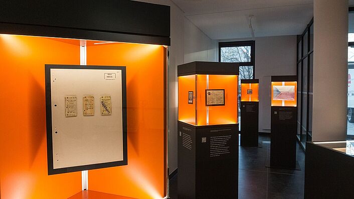 Blick in die Wanderausstellung. Zu sehen sind mehrere Stelen mit Glasvitrinen, in denen sich Dokumente, Fotos und Objekte befinden.